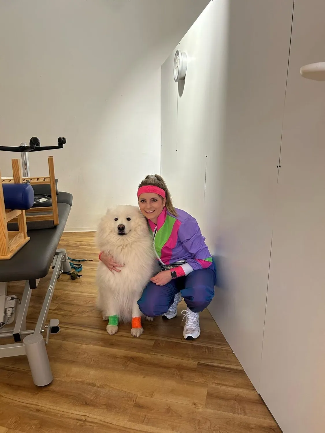 Kollegin im bunten Sportoutfit mit Hund in einem Behandlungsraum bei AMILU in Oberursel